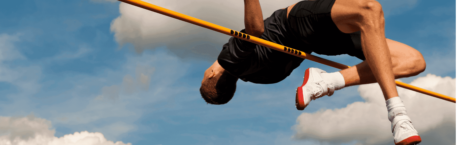 Ein Athlet in Sportkleidung überspringt eine Hochsprunglatte vor einem blauen Himmel mit Wolken