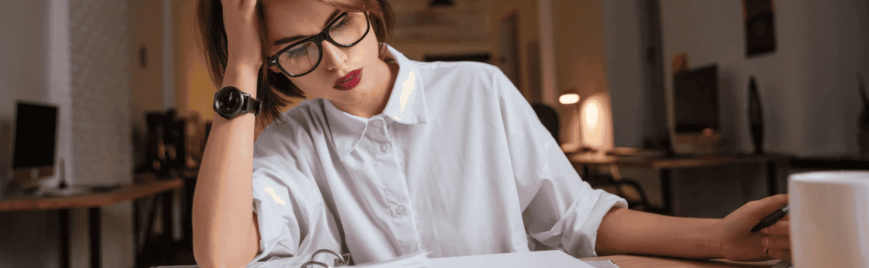 Frau sitzt mit Kopfschmerzen am Schreibtisch